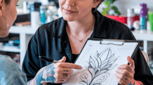 Jovem escolhendo design para primeira tatuagem com ajuda profissional.