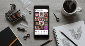 Mesa de trabalho de tatuador com smartphone exibindo feed de Instagram com tatuagens, máquina de tatuar e materiais de desenho, simbolizando o marketing para tatuadores.