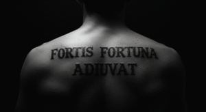 Tatuagem com a frase em latim "Fortis Fortuna Adiuvat" nas costas, com uma fonte de estilo romano, transmitindo seu significado de força.