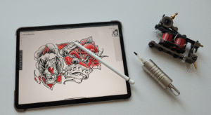 Mesa de um tatuador com um iPad mostrando um desenho no Procreate, o melhor aplicativo para desenhar tatuagem, ao lado de uma máquina de tatuar.