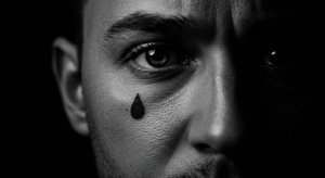 Close-up do rosto de um homem com uma tatuagem de lágrima preenchida, ilustrando o significado pesado e complexo do símbolo.