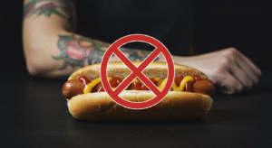 Imagem de um cachorro-quente com um sinal de proibido, ilustrando que não se pode comer salsicha depois de tatuar.